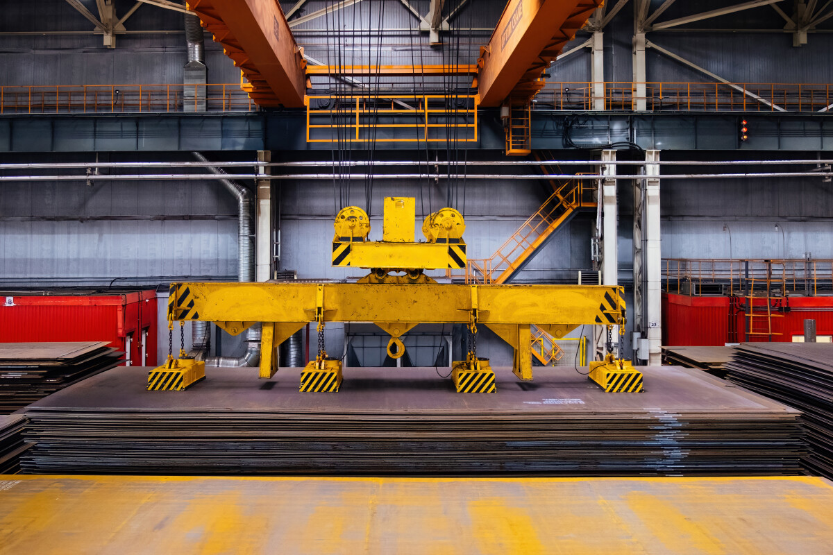 Overhead crane with magnetic grippers lifting steel sheets