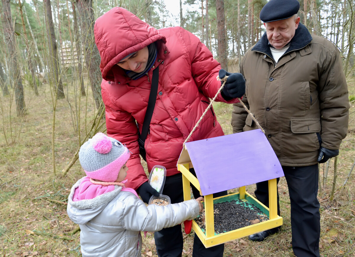 Молодой человек с дочерью и дедушкой насыпали зерна в кормушку для птиц