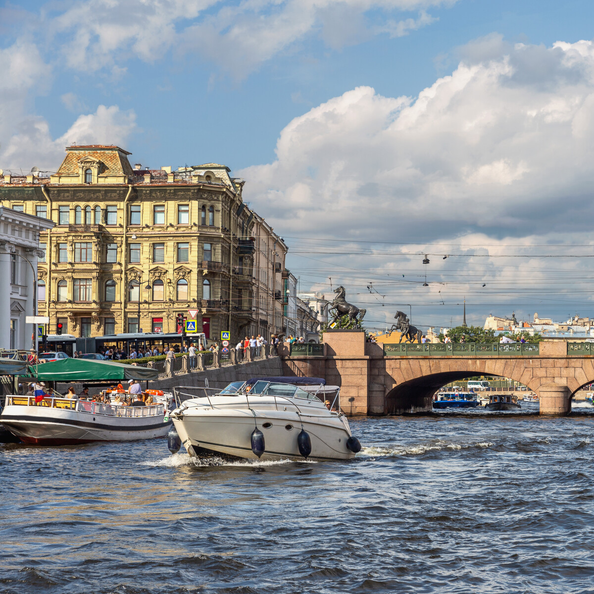 Туристы на прогулочных катерах плывут по каналу в центре города на фоне Аничкина моста в Санкт-Петербурге