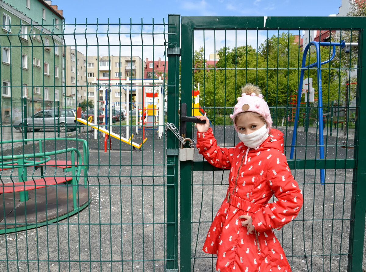 Девочка в медицинской маске стоит возле закрытой детской площадки. В России эпидемия коронавируса COVID-19. Калининград