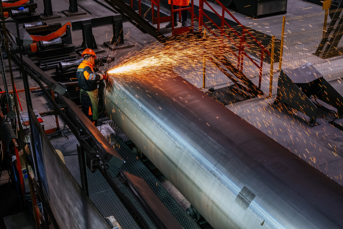 Worker cleans welded seam on steel pipe using grinding machine