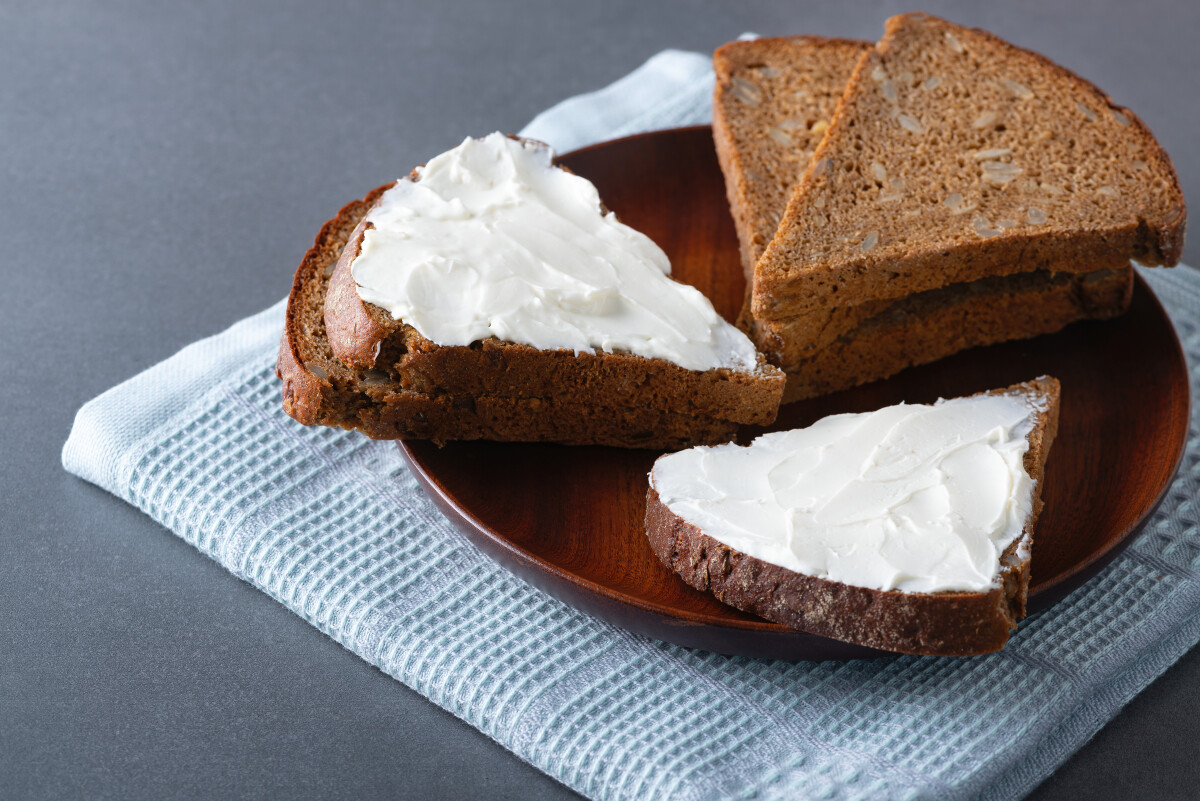 Ржаной хлеб со сливочным сыром на деревянной тарелке, деревенская кухня