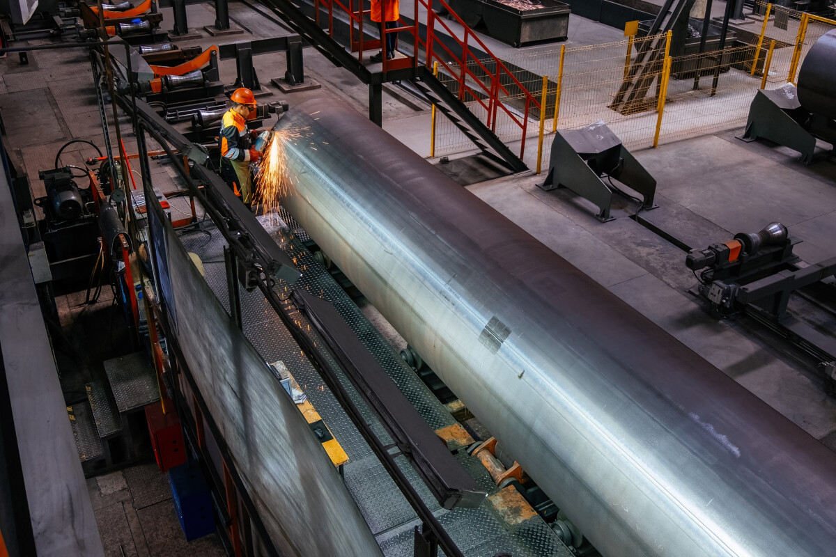 Worker cleans welded seam on steel pipe using grinding machine