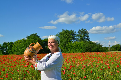 Сельская женщина пьет воду из кувшина на маковом поле
