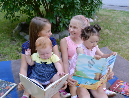 КАЛИНИНГРАД, РОССИЯ - 28 июня 2018 года: Маленькие девочки рассматривают книги, сидя на коленях у старших сестер