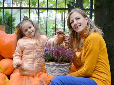 Мама и ее дочь держат корзину с мечами на фоне оранжевой тыквы. Семейный портрет